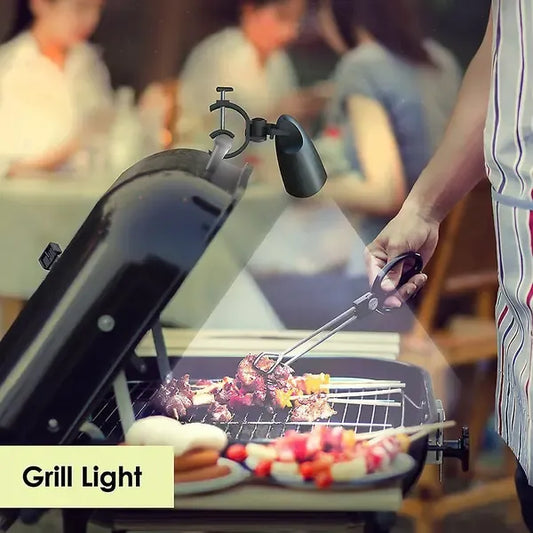 Black clip-on LED grill light clamped to a barbecue handle at night