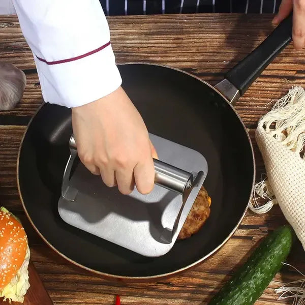 Square stainless steel burger press with round handle on a hot flat top