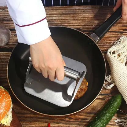 Square stainless steel burger press with round handle on a hot flat top