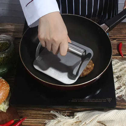 Square stainless steel burger press with round handle on a hot flat top