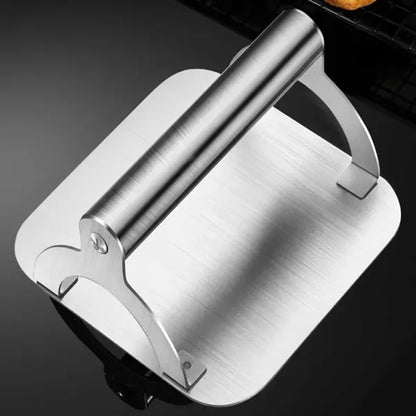 Square stainless steel burger press with round handle on a hot flat top