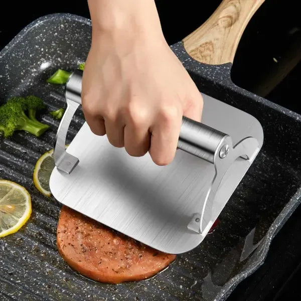 Square stainless steel burger press with round handle on a hot flat top