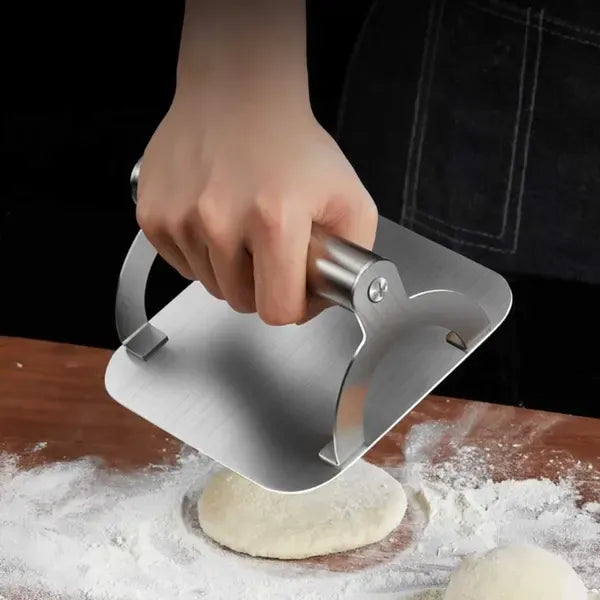 Square stainless steel burger press with round handle on a hot flat top