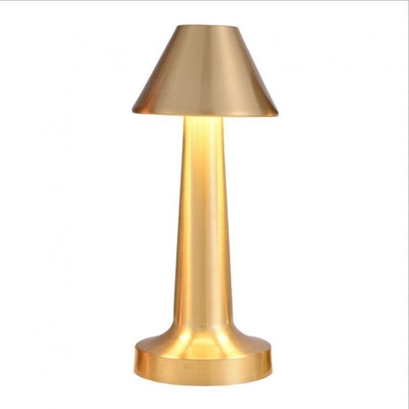 Gold dumbbell-shaped cordless lamp lit on a vanity table