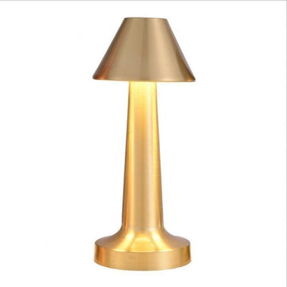 Gold dumbbell-shaped cordless lamp lit on a vanity table