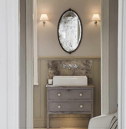 Pair of chrome wall sconces with white linen shades lit on a bedroom wall