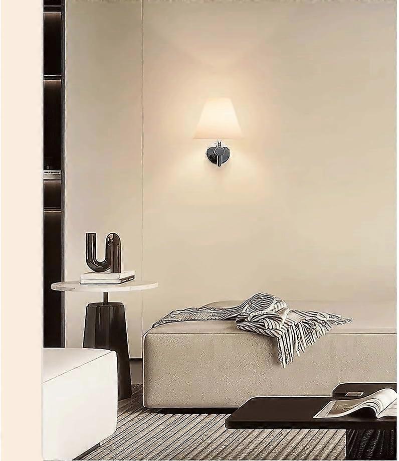 Pair of chrome wall sconces with white linen shades lit on a bedroom wall