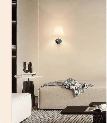 Pair of chrome wall sconces with white linen shades lit on a bedroom wall