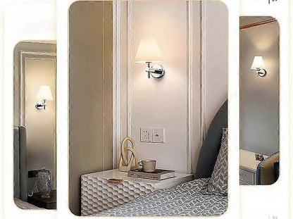 Pair of chrome wall sconces with white linen shades lit on a bedroom wall