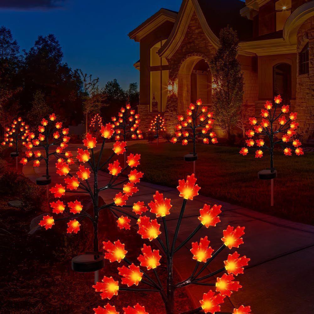 Three solar maple leaf stake lights glowing warm amber in a garden setting