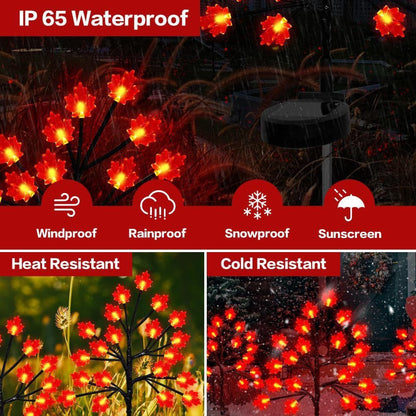 Three solar maple leaf stake lights glowing warm amber in a garden setting