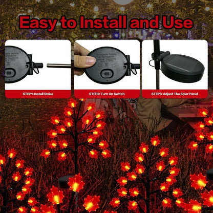 Three solar maple leaf stake lights glowing warm amber in a garden setting