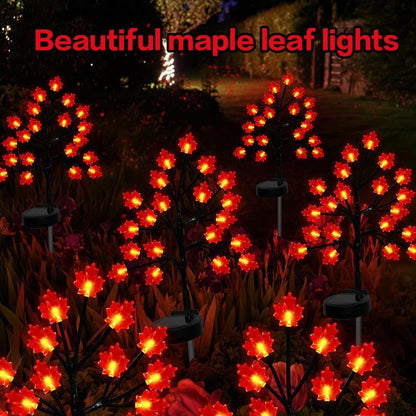 Three solar maple leaf stake lights glowing warm amber in a garden setting