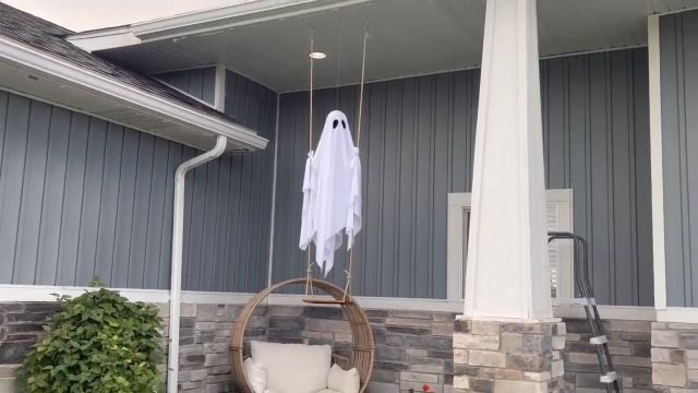 White fabric Halloween ghost hanging from a porch and lit from within