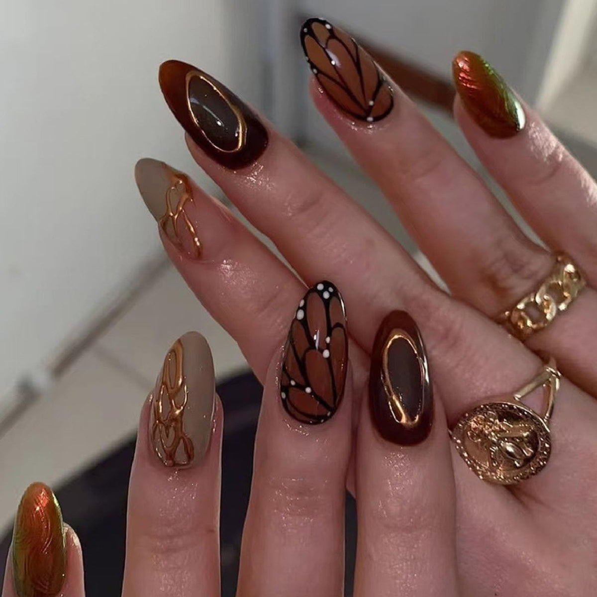 Brown medium almond press-on nails with butterfly wing designs and chrome accents