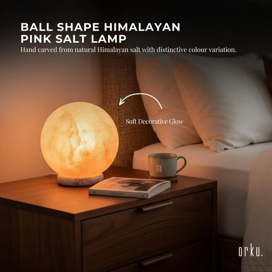 Carved sphere Himalayan pink salt lamp glowing amber on a timber base