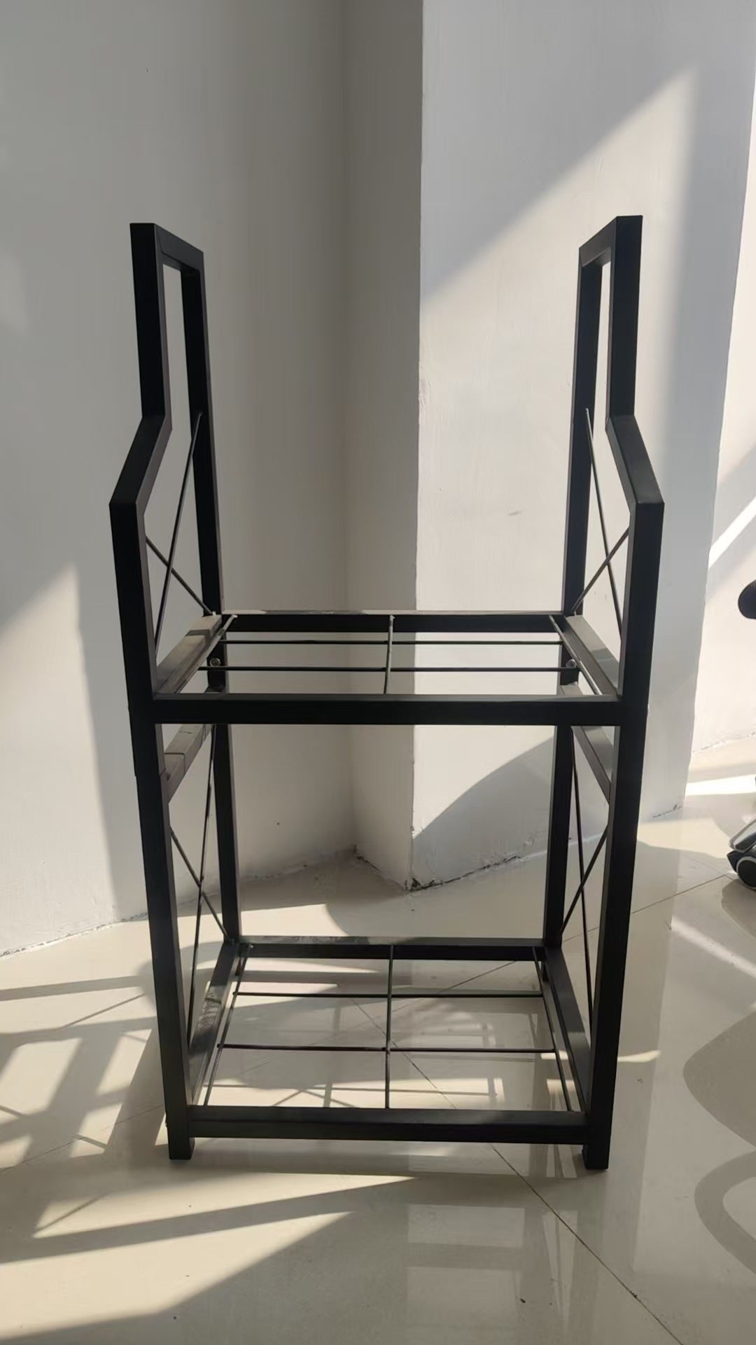 Two tier black metal firewood rack holding split logs beside a fireplace