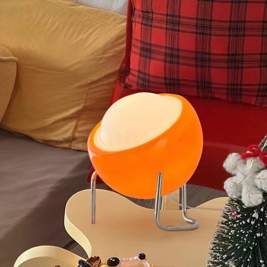 Small orange glass and iron table lamp glowing warm on a shelf