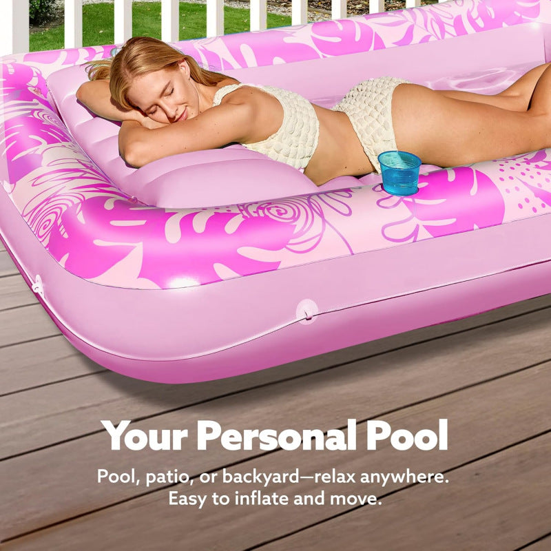 Pink inflatable suntan tub with pillow and cup holders on a lawn